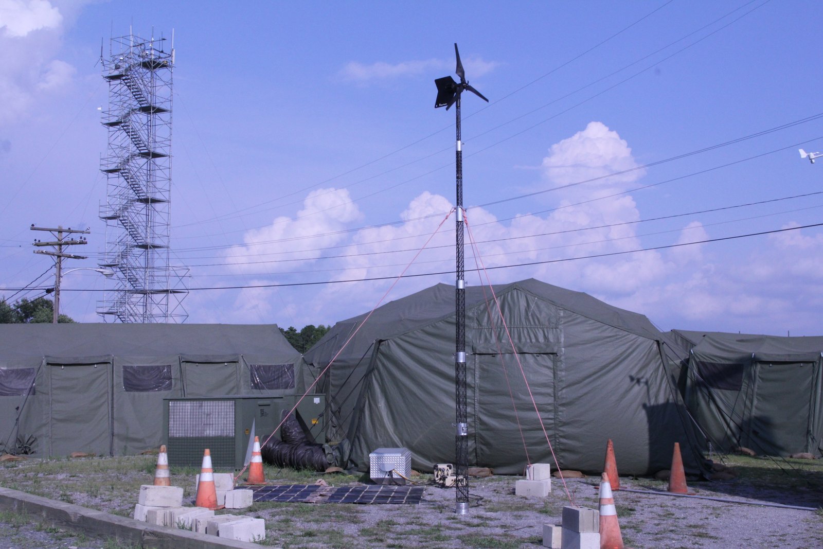 A tactical microgrid with a small wind turbine and solar panels beside Army tents at Fort Dix, New Jersey.
