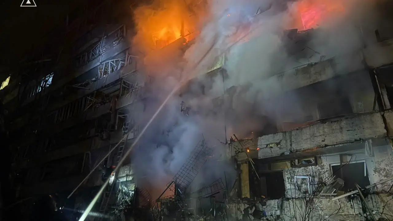 Firefighters spray water on a burning, partly collapsed apartment building in Kyiv at night after the Russian attack of Oct 13, 2026, with flames in the upper floors.